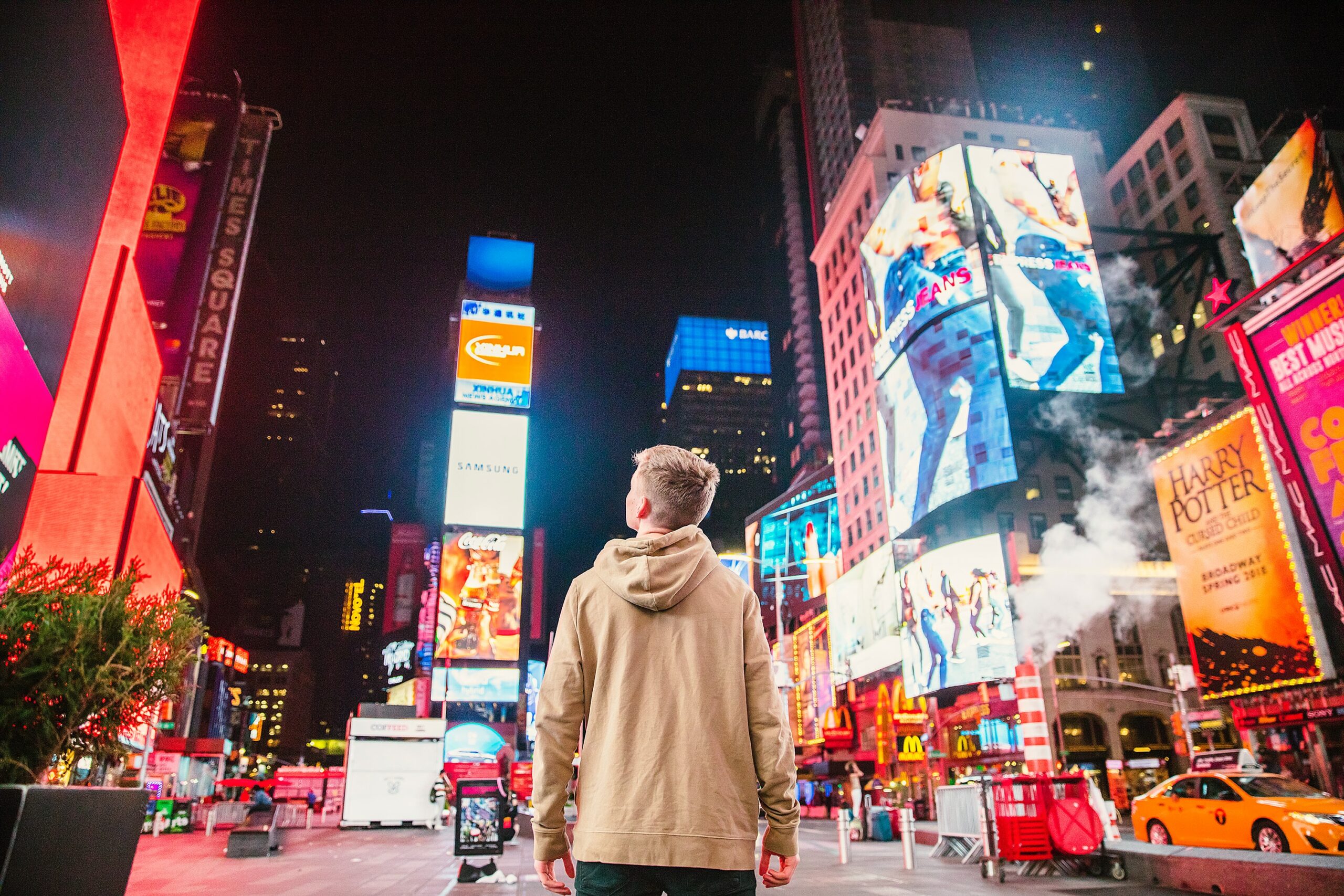 boy in the middle of the city watching huge buildings with electonic advertisments on them
