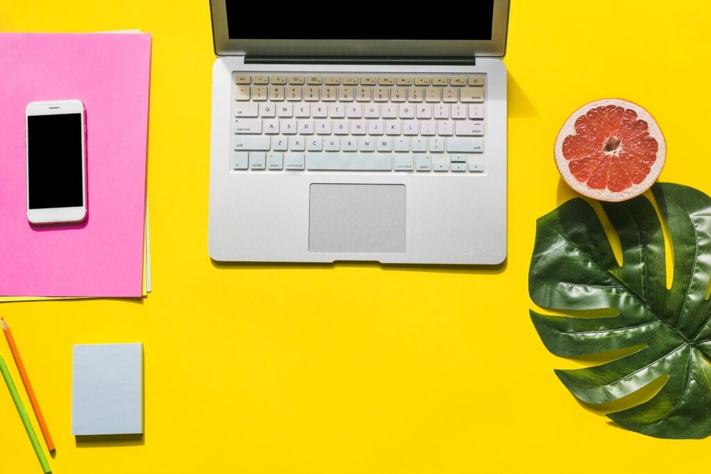 office laptop on yellow table with mobile phone nearby and colorful elements